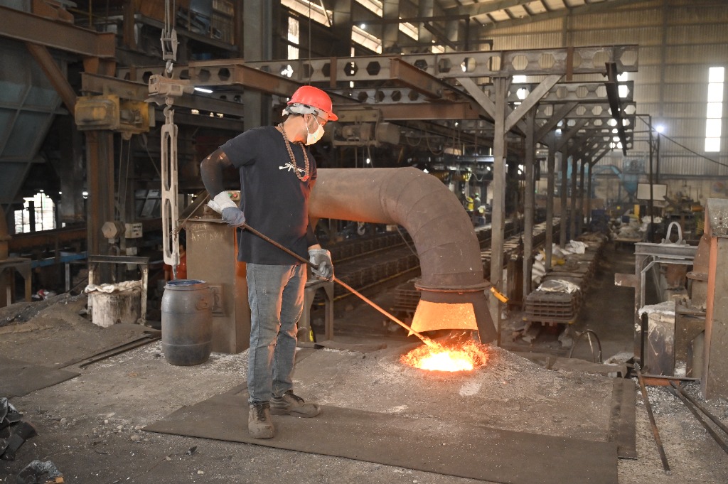 Skilled induction furnace operator slagging molten grey and ductile iron