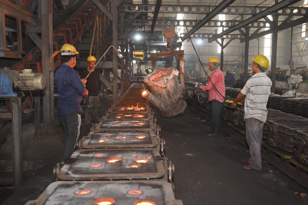 Pouring crew casting molten iron from ladle into mould boxes on loop conveyor line